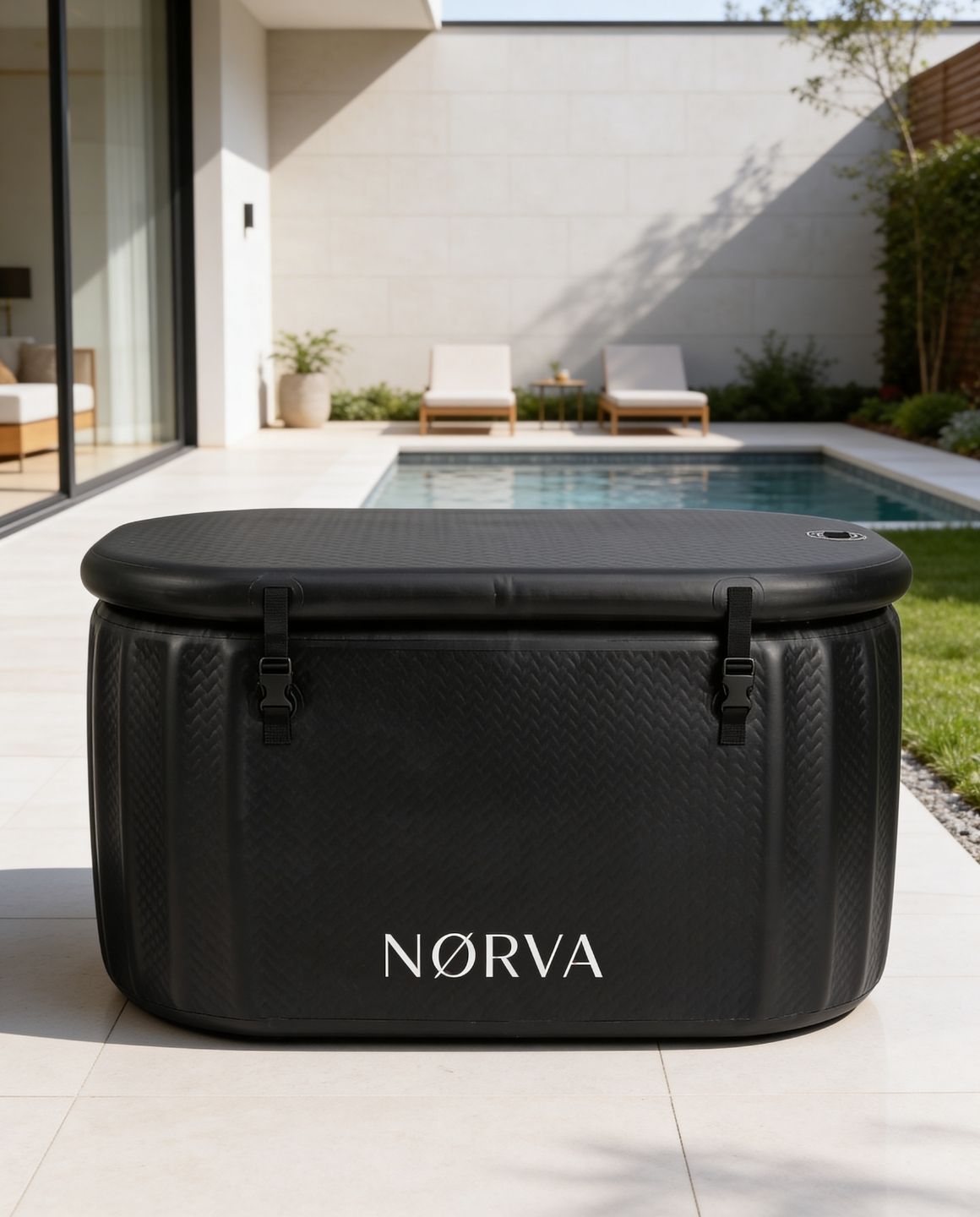 Black Nørva ice bath on a patio with a pool and chairs in the background